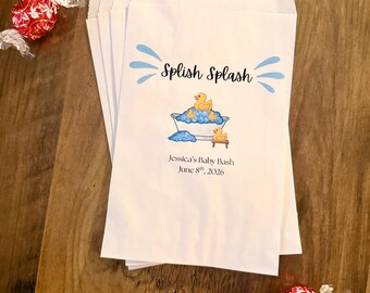 Puede incluir: Una pila de bolsas de papel blanco con un gráfico azul de una bañera con patitos de goma amarillos y burbujas azules. El texto dice Splish Splash, Jessica's Baby Bash y June 8th, 2026. Dos caramelos envueltos en rojo están colocados cerca.