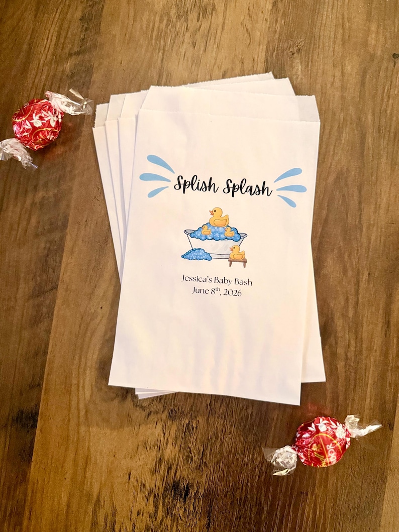 Pode incluir: Uma pilha de sacos de papel branco com um gr&aacute;fico azul de uma banheira com patinhos de borracha amarelos e bolhas azuis. O texto diz Splish Splash, Jessica's Baby Bash e June 8th, 2026. Dois doces embrulhados em vermelho est&atilde;o pr&oacute;ximos.