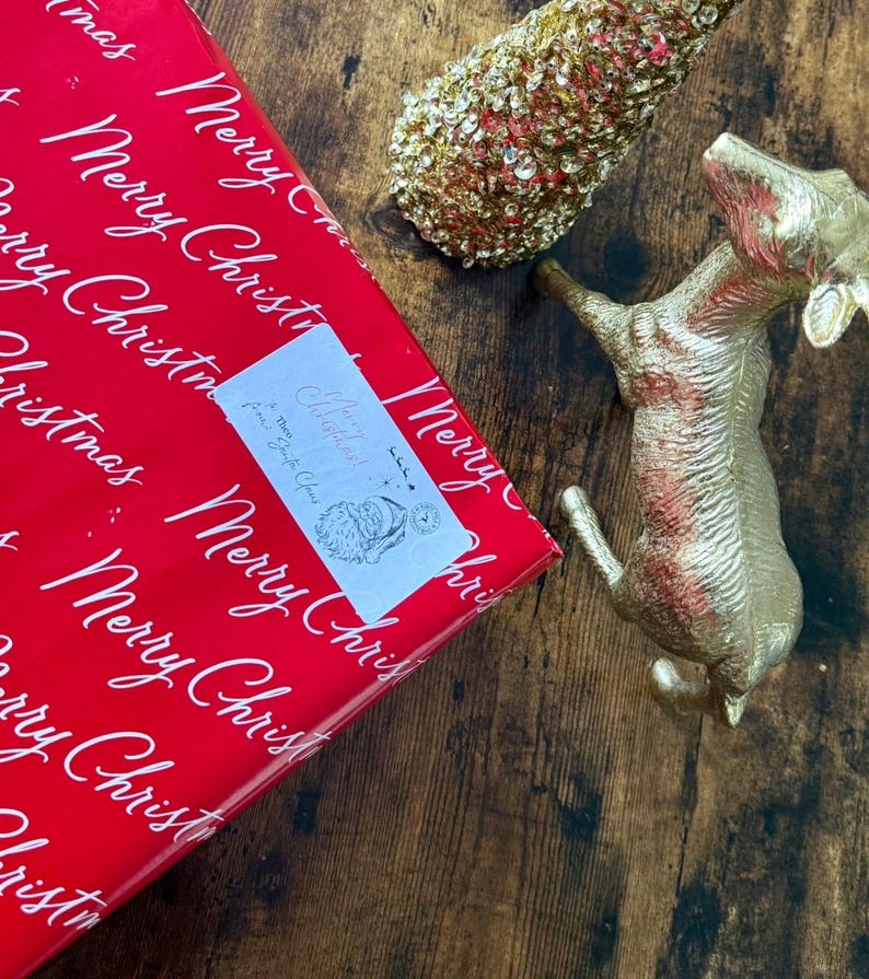 May include: A Christmas-themed image with a red gift box printed with white "Merry Christmas" text, a gold dog ornament, and a gold Christmas tree decoration. A small label on the gift box reads "Merry Christmas! From Santa Claus".