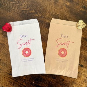 May include: Two paper treat bags, one white and one tan, with a pink donut graphic and the words "Two Sweet". Text at the bottom reads "Thanks for celebrating Jessica's Birthday!". A red heart-shaped candy and a gold heart-shaped candy are on the bags.