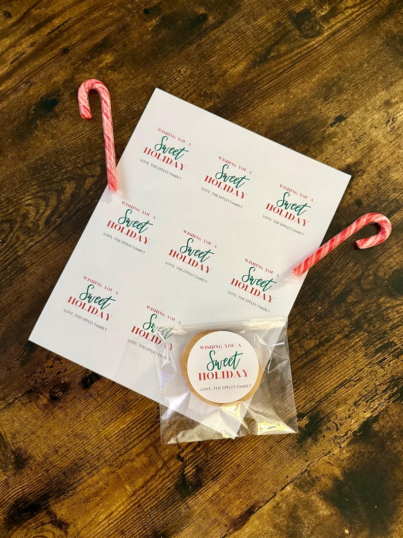 May include: A holiday-themed image featuring a sheet of stickers and a cookie in a clear bag. The stickers and cookie have the text "Wishing You a Sweet Holiday" in green and red. Two red and white candy canes are also present.