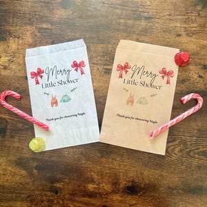 May include: Two paper gift bags with the text "Merry Little Shower" and baby clothes illustrations. Red bows and the text "Thank you for showering Kayla" are also printed on the bags. Candy canes and a gold sequin are also visible.