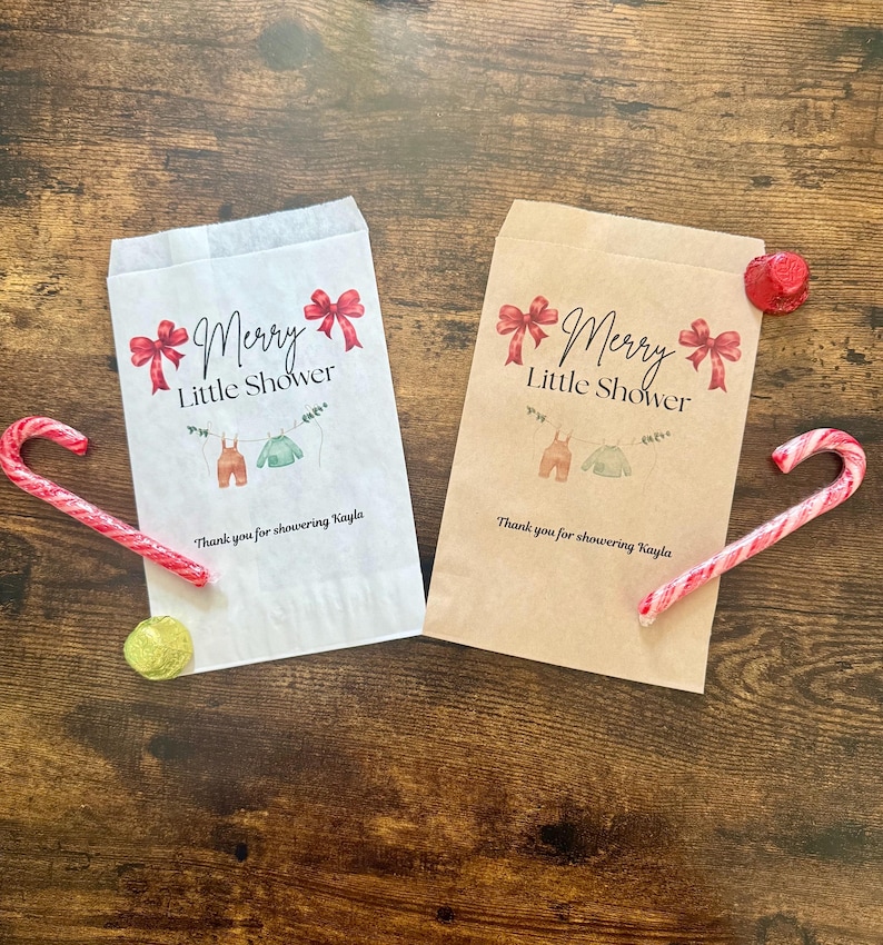 May include: Two paper gift bags with the text "Merry Little Shower" and baby clothes illustrations. Red bows and the text "Thank you for showering Kayla" are also printed on the bags. Candy canes and a gold sequin are also visible.