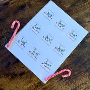 May include: A sheet of white paper with the text "Wishing You a Sweet Holiday" in red and green, along with two red and white striped candy canes on a wooden surface. The text also includes "Love, The Eppley Family."