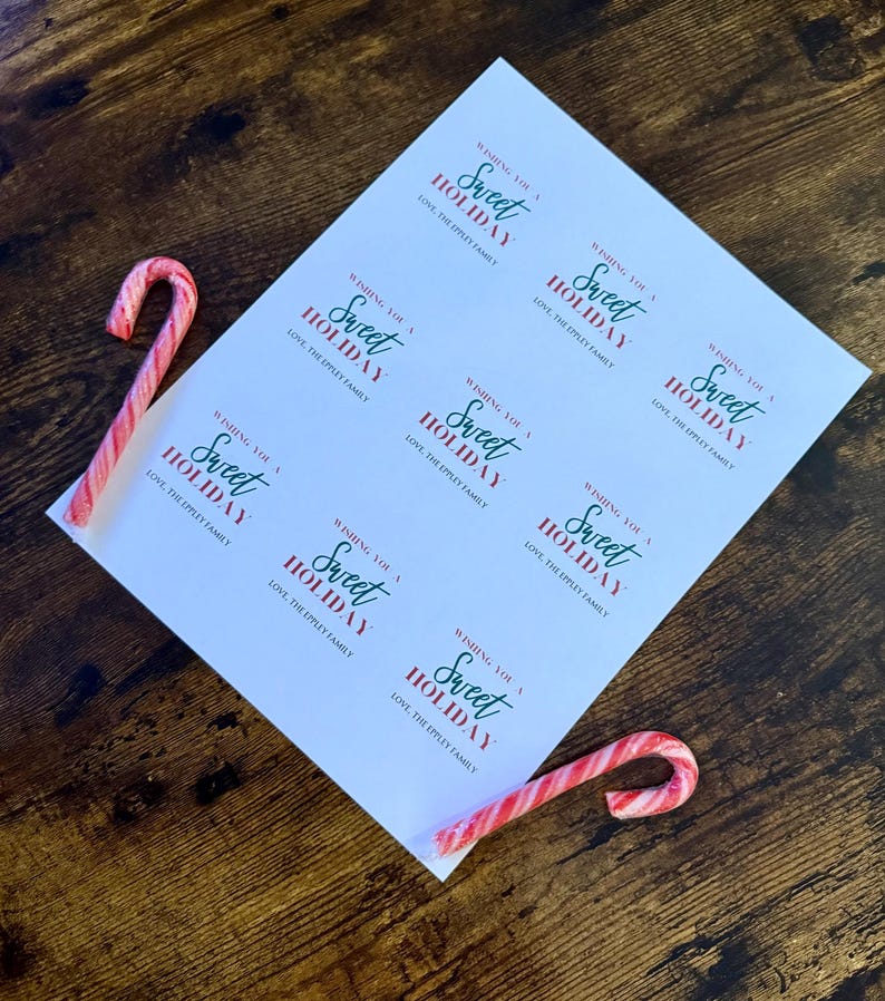 May include: A sheet of white paper with the text "Wishing You a Sweet Holiday" in red and green, along with two red and white striped candy canes on a wooden surface. The text also includes "Love, The Eppley Family."