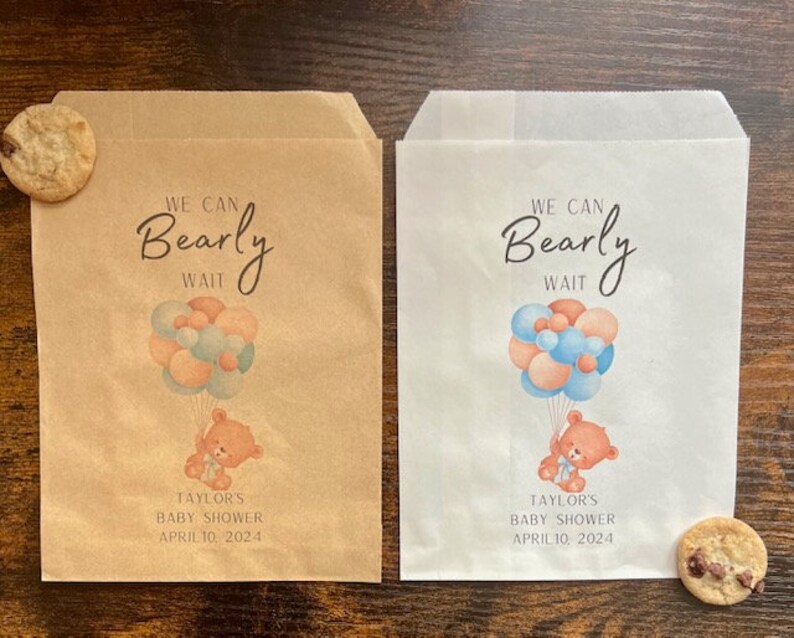 May include: Two paper treat bags, one brown and one white, with a baby shower design. Each bag features a teddy bear holding balloons and the text "We Can Bearly Wait." The date "April 10, 2024" is also printed on the bags.