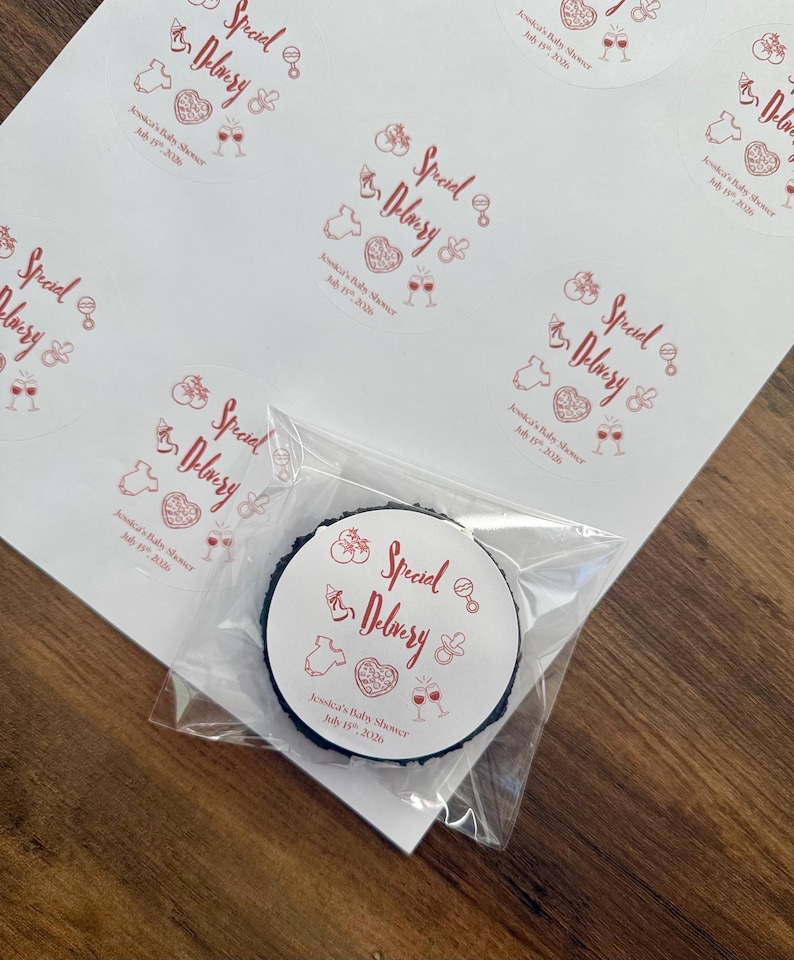 Op de afbeelding: Een vel met ronde witte stickers met rode inkt met de tekst Special Delivery, Jessica's Baby Shower, July 19th, 2026, en iconen van een babyfles, rammelaar, rompertje, hart en twee glazen. E&eacute;n sticker zit in een doorzichtig plastic zakje.