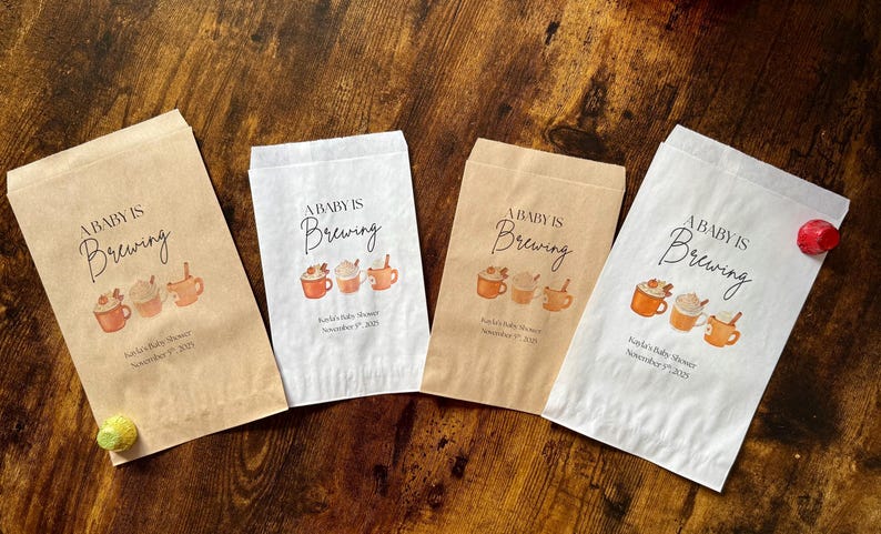 May include: Four paper favor bags with the text "A Baby is Brewing" and a watercolor illustration of coffee cups. The bags are in shades of brown and white, with a baby shower date printed on them.