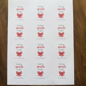 May include: A sheet of twelve circular white stickers, each featuring a red bow illustration, the text 'baking spirits bright' in dark gray and red, and the personalized text 'Love, The Smith Family' at the bottom of each label.