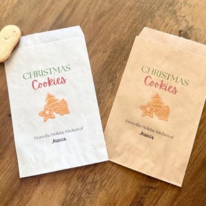 May include: Two rectangular paper bags, one white and one brown, each printed with the text "CHRISTMAS Cookies" in green and red, a graphic of three cookies, and the text "From the Holiday Kitchen of Jessica" in black ink.