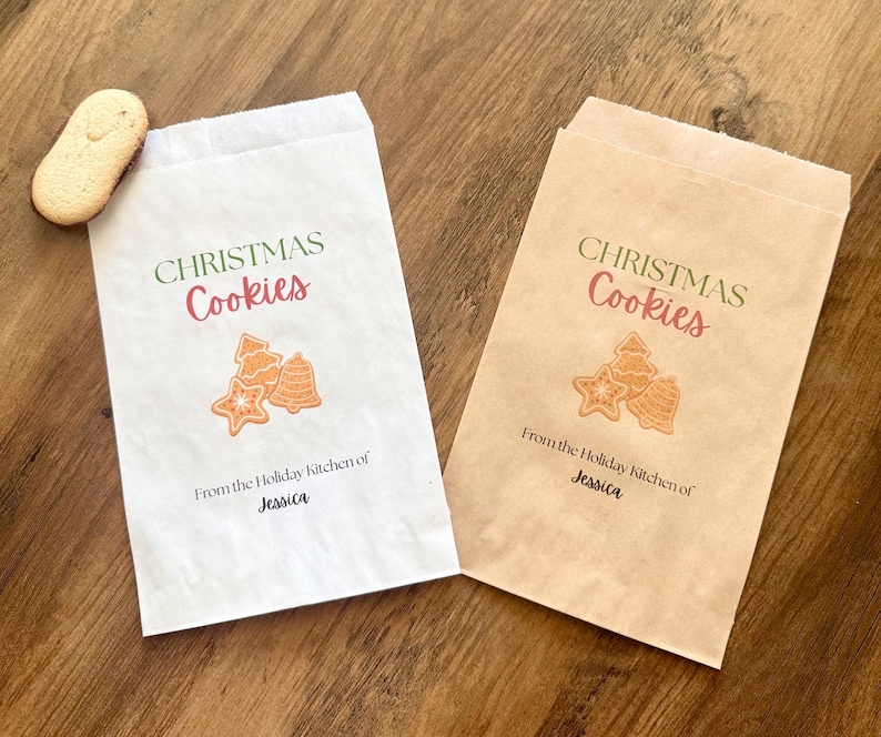 May include: Two rectangular paper bags, one white and one brown, each printed with the text "CHRISTMAS Cookies" in green and red, a graphic of three cookies, and the text "From the Holiday Kitchen of Jessica" in black ink.