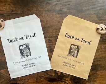 May include: Two Halloween-themed treat bags, one white and one brown, with the text "Trick or Treat". Each bag features a skeleton couple graphic and the message "Love is sweet, enjoy a treat". A cookie rests on each bag.