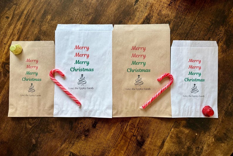 May include: Four paper gift bags, two white and two brown, with "Merry Christmas" printed in red and green. Each bag has a candy cane or a red ornament. The bags are arranged on a wooden surface.