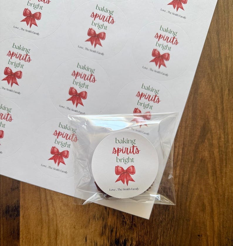 May include: A sheet of circular white stickers featuring the text baking spirits bright in green and red script, accompanied by a red bow illustration and the text Love, The Smith Family. One sticker is individually wrapped in clear plastic.