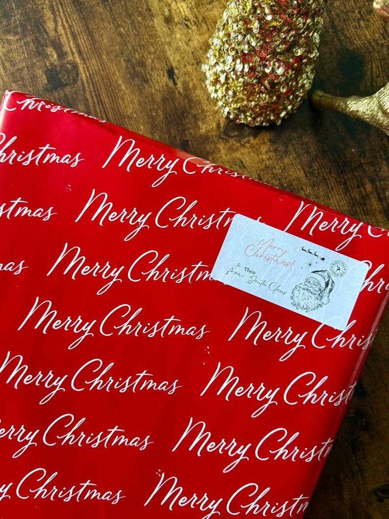 May include: A Christmas gift wrapped in red paper with a repeating white script of "Merry Christmas". A small label reads "Merry Christmas! from Santa Claus" with a Santa illustration. Festive holiday theme.