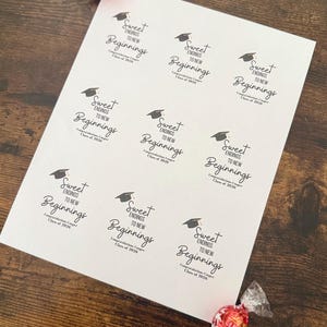K&ouml;nnte beinhalten: Ein wei&szlig;es Blatt Papier mit dem Text "Sweet Endings to New Beginnings" und einer Abschlusskappe. Der Text enth&auml;lt "Class of 2020". Zwei verpackte S&uuml;&szlig;igkeiten befinden sich im Bild. Das Papier liegt auf einer Holzoberfl&auml;che.
