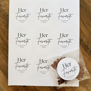 Peut inclure: Une feuille de papier blanc avec huit autocollants circulaires portant le texte noir Her Favorite, Jessica & Dave, et 07.14.26. Un autocollant suppl&eacute;mentaire est coll&eacute; sur un sachet plastique transparent contenant des petits &eacute;l&eacute;ments bruns.