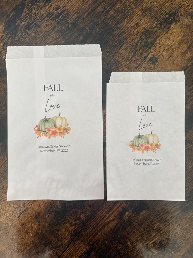 May include: Two white paper treat bags with the text "FALL in Love" and a watercolour illustration of pumpkins and flowers. The text "Jessica's Bridal Shower November 12th, 2025" is printed below the illustration.