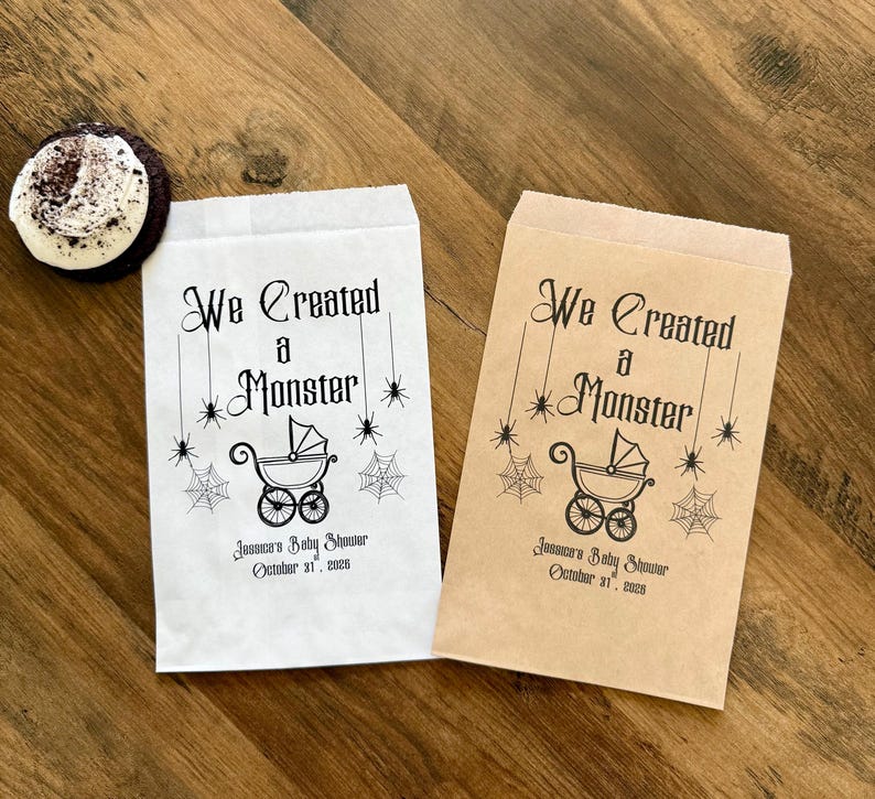 May include: Two rectangular paper favor bags, one white and one brown, each printed with black ink featuring the text We Created a Monster, a baby carriage illustration, spider webs, and spiders, plus Jessica's Baby Shower October 31, 2025.
