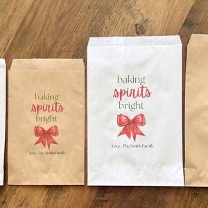 May include: Four rectangular paper bags in white and brown kraft paper. Each bag features the text 'baking spirits bright' in green and red, a red bow illustration, and the personalised text 'Love, The Smith Family' at the bottom.