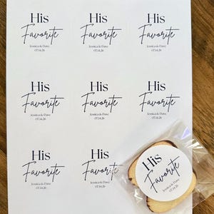 Peut inclure: Une feuille blanche pr&eacute;sentant neuf &eacute;tiquettes adh&eacute;sives circulaires avec le texte noir His Favorite, Jessica & Dave, et 07.14.26. Une &eacute;tiquette identique est appos&eacute;e sur un petit biscuit rond clair dans un sachet en plastique transparent.