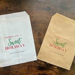 May include: Two paper cookie bags, one white and one brown, with a chocolate chip cookie on each. The bags have the text "Wishing You a Sweet Holiday" in green and red, and "Love, The Eppley Family" in black.