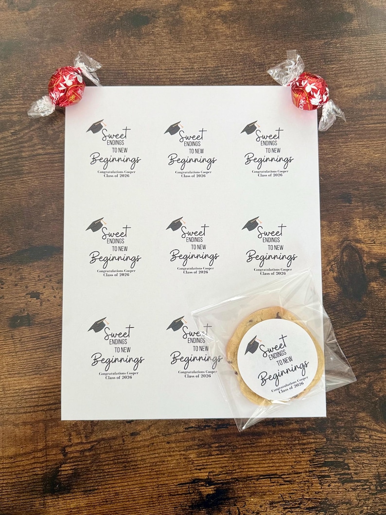 K&ouml;nnte beinhalten: Ein Bogen wei&szlig;er Aufkleber mit dem Text "Sweet Endings to New Beginnings" und einer Abschlusskappe. Ein Schokoladen-Chip-Keks in einer durchsichtigen T&uuml;te und zwei rot folienverpackte S&uuml;&szlig;igkeiten sind ebenfalls vorhanden. Der Text "Congratulations Cooper Class of 2026" ist ebenfalls auf den Aufklebern.
