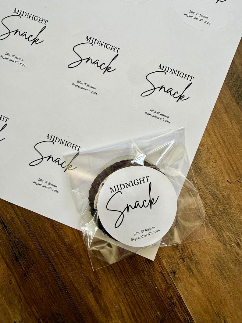 May include: A sheet of circular white adhesive labels featuring the black printed text Midnight Snack and John & Jessica September 5th, 2026. One label is applied to a clear plastic bag containing a dark round cookie with a white cream filling.