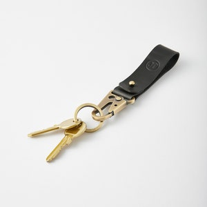 Peut inclure: Porte-clés en cuir noir avec un anneau de clé en laiton et deux clés en laiton. La sangle en cuir a un petit cercle avec la lettre "J" en relief.