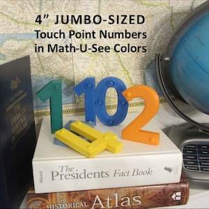 May include: Colorful 4-inch (10 cm) jumbo-sized touch point numbers in green, blue, and orange, along with yellow math symbols, are displayed on a stack of books. The text on the image reads "4" JUMBO-SIZED Touch Point Numbers in Math-U-See Colors."