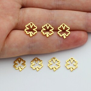 May include: Six gold-colored metal charms shaped like four-leaf clovers. The charms are arranged in two rows on a hand.