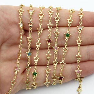 May include: Gold-colored star chain with colorful gemstone accents. The chain features small, open star shapes linked together, each holding a different colored gemstone. The gemstones include pink, green, blue, and red.