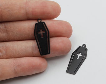 May include: Two black metal coffin charms with a cross cutout. The charms are about 2 inches long and have a hole at the top for attaching to a chain or bracelet.