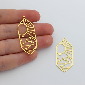 May include: Two gold-toned metal charms in the shape of a geometric crystal with a sun and moon design. The sun has rays and the moon has a cloud and stars.