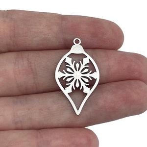 May include: Silver metal Christmas ornament charm with a snowflake cutout design.