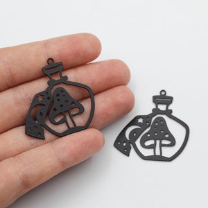 May include: Two black metal charms shaped like bottles with a mushroom and moon design. The charms have a hole at the top for attaching to a necklace or bracelet.
