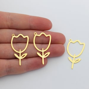 Könnte beinhalten: Drei goldfarbene, tulpenförmige Anhänger. Die Anhänger sind aus dünnem Metall gefertigt und haben ein einfaches, umrissenes Design. Jeder Anhänger zeigt eine Tulpenblume mit Stiel und Blättern. Die Anhänger werden vor einem weißen Hintergrund gezeigt.