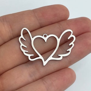 Pode incluir: Encanto de prata com formato de coração com asas. O encanto é um design recortado.