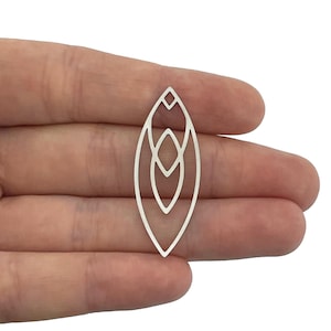 Puede incluir: Un colgante de metal plateado con un diseño geométrico. El colgante tiene forma ovalada con tres círculos concéntricos en su interior.