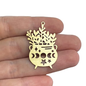 May include: Gold metal charm featuring a cauldron with a crescent moon and star design. The cauldron is filled with a leafy plant.