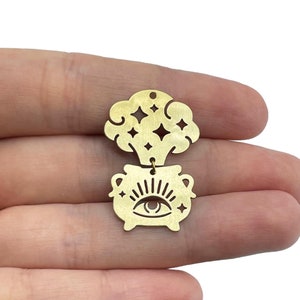 Puede incluir: Encanto de metal dorado con un caldero con un solo ojo y una nube de estrellas arriba.