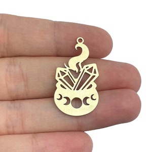 Puede incluir: Encanto de metal dorado con un caldero con tres lunas crecientes, dos cristales y una llama.