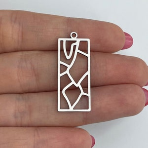 May include: Silver pendant featuring a geometric design. The pendant is rectangular and has a hole at the top for hanging.