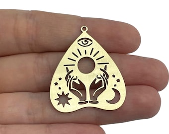 May include: Gold-toned metal charm in the shape of a heart with a sun, moon, and stars design. The charm features two hands holding the sun, with an eye in the centre of the sun.