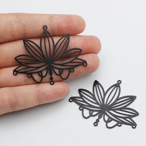 May include: Two black metal lotus flower charms with intricate cut-out designs. The charms have a delicate, filigree look and are perfect for adding a touch of elegance to jewelry projects.