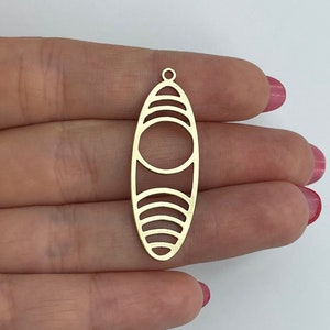 May include: Gold-toned metal pendant with a geometric design featuring a large oval shape with concentric circles inside. The pendant has a hole at the top for attaching a chain or cord.