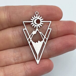 May include: Silver pendant charm featuring a geometric triangle design with a mountain, sun, and moon inside.