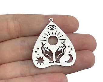 May include: Silver charm in the shape of a Ouija board planchette with an all-seeing eye, sun, moon, and stars.