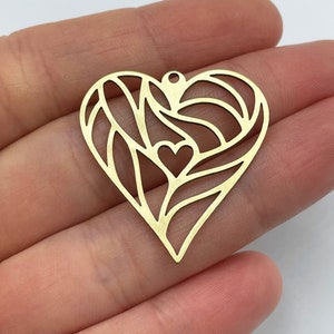 Op de afbeelding: Gouden metalen hartbedel met een delicaat, ingewikkeld ontwerp. Het hart heeft een kleinere hartuitsparing in het midden.