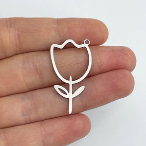 May include: Silver metal charm shaped like a simple outline of a tulip flower. The charm has a hole at the top for attaching to jewelry or other crafts.